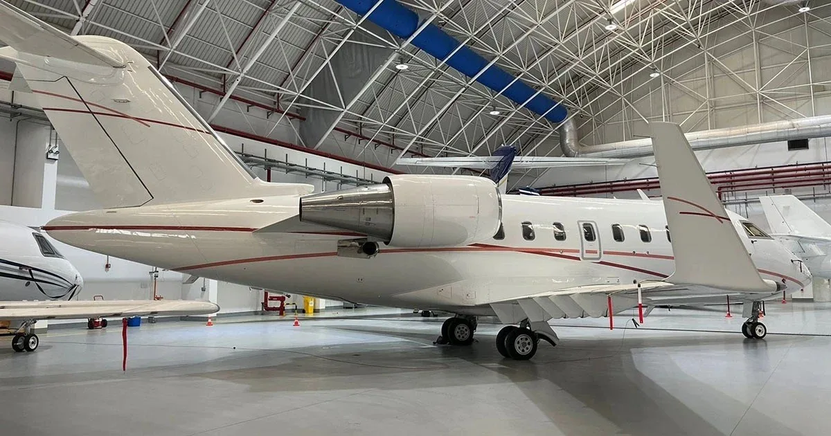A white business jet with red pinstripes parked inside a hangar, viewed from the rear-right.