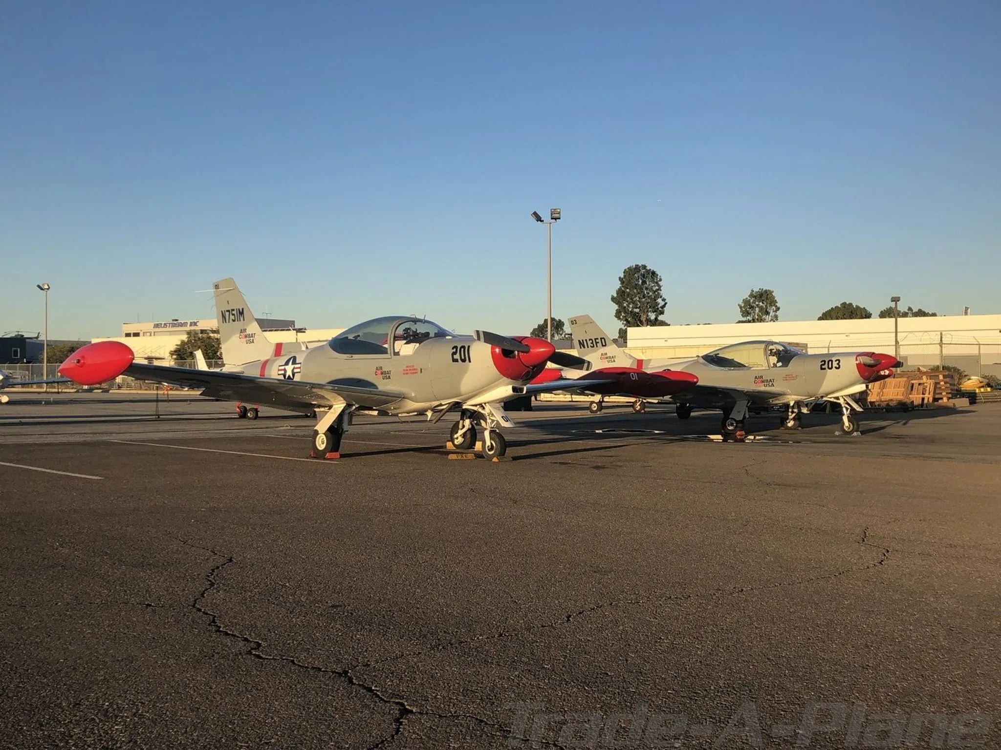 Two gray and red single-engine aircraft, N751M and N13FD, are parked on an asphalt tarmac at an airport.