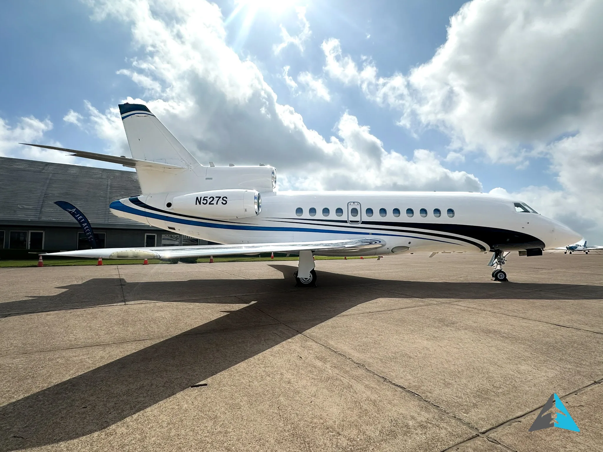 A side view of a white Dassault Falcon 900EX business jet with black and blue stripes, parked on an airfield.