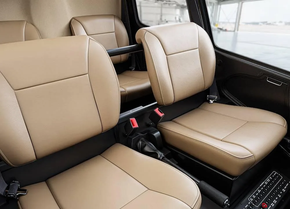 Tan leather passenger seats in the cabin of a helicopter, with a view of a hangar outside.