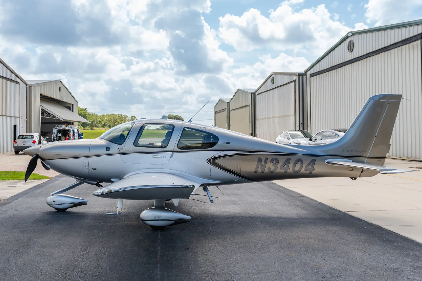 Side view of a silver Cirrus SR22T aircraft (N3404) parked on an airport tarmac with hangars in the background.