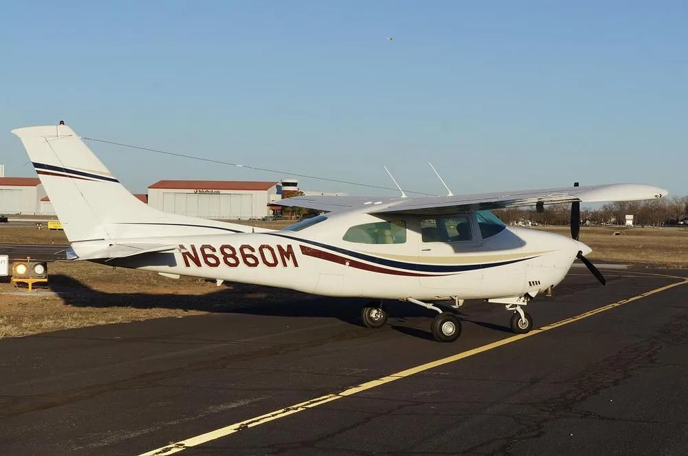 A white Cessna 210 Centurion aircraft with red, blue, and gold stripes parked on an airfield.