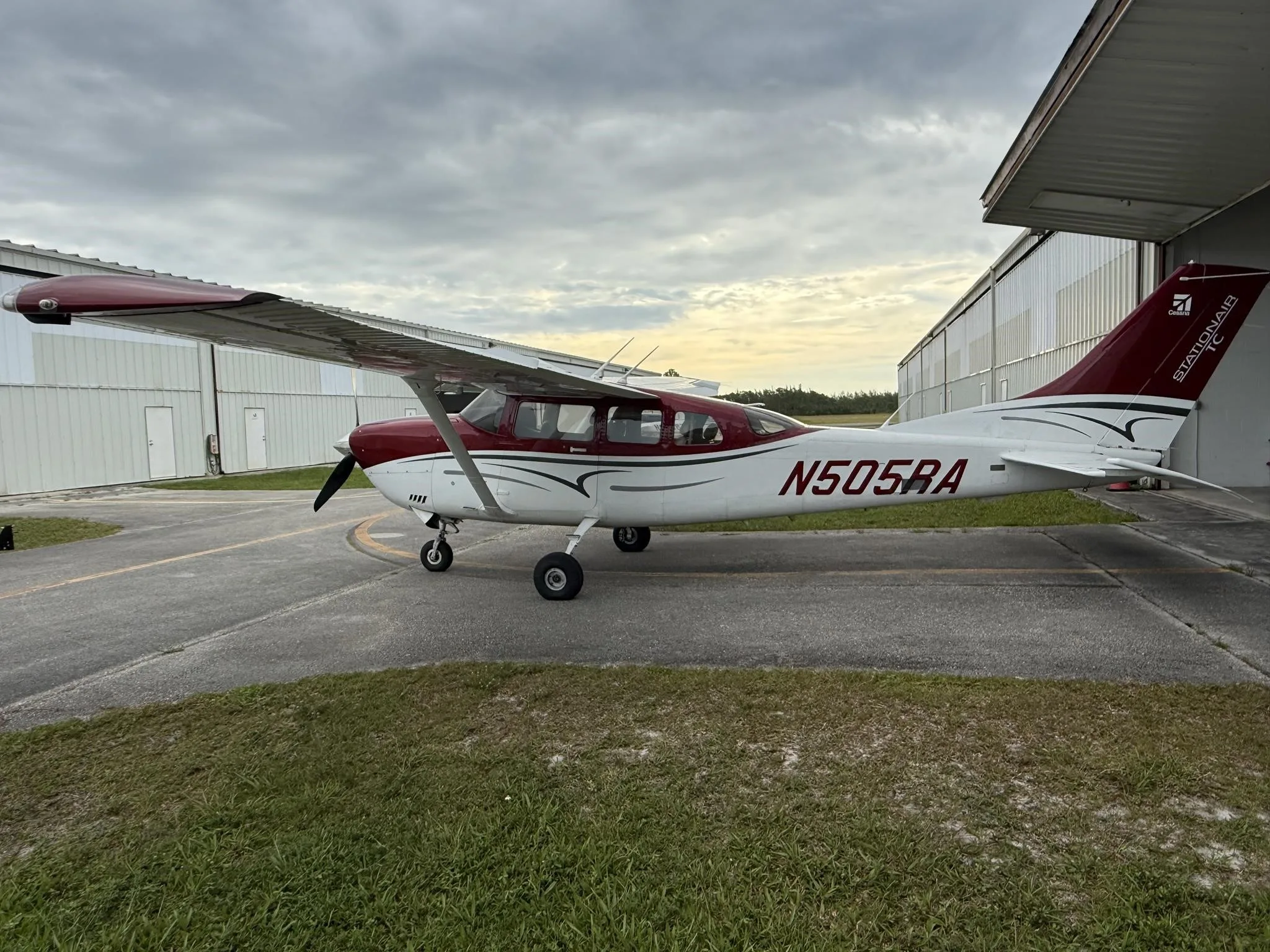 A red and white Cessna Stationair TC aircraft (N505RA) parked outside a hangar, viewed from the rear left.
