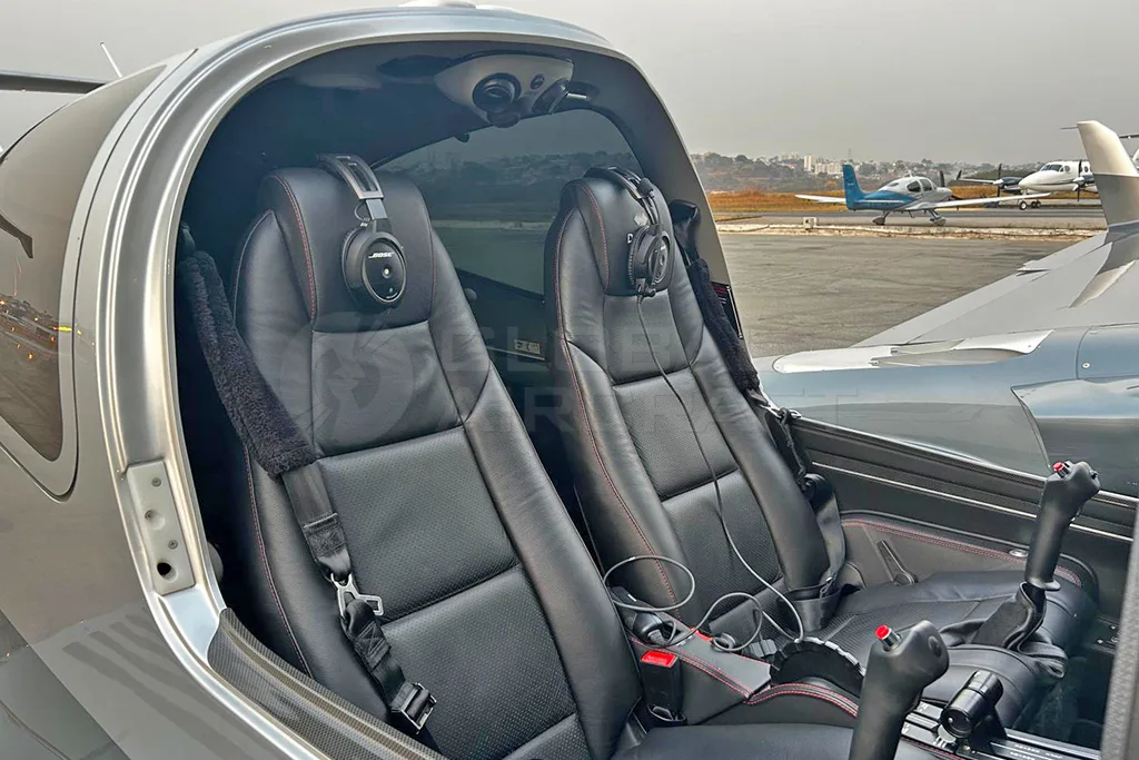 The front interior cabin of a Diamond DA62 aircraft with two black leather seats and headsets, looking out towards the tarmac.