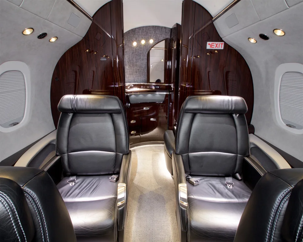 A view down the aisle of a private jet cabin towards the rear galley and lavatory area.