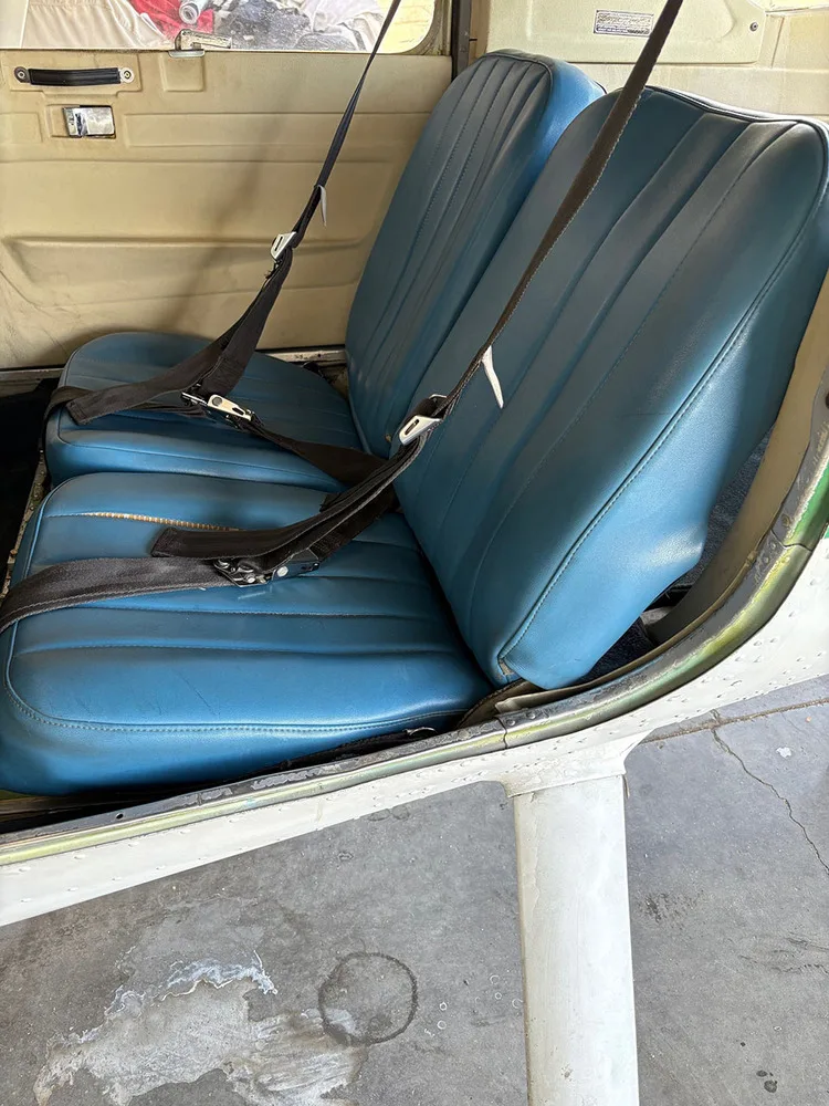 A close-up view of two blue vinyl passenger seats with seatbelts in the aircraft cabin.