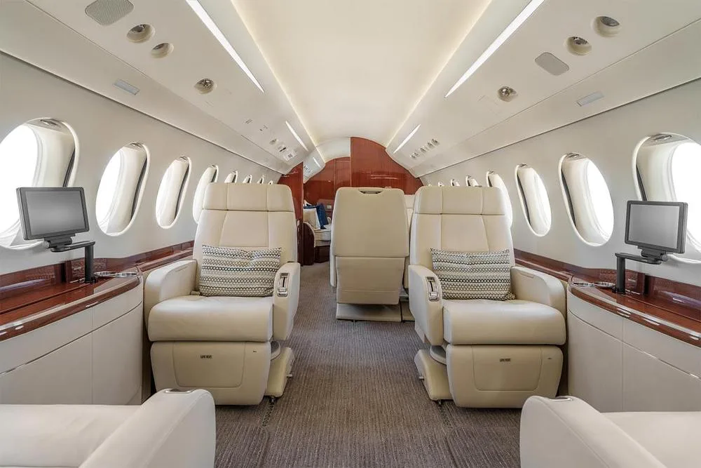 The luxurious cabin interior of a business jet, featuring cream leather seats, wood paneling, and individual entertainment screens.