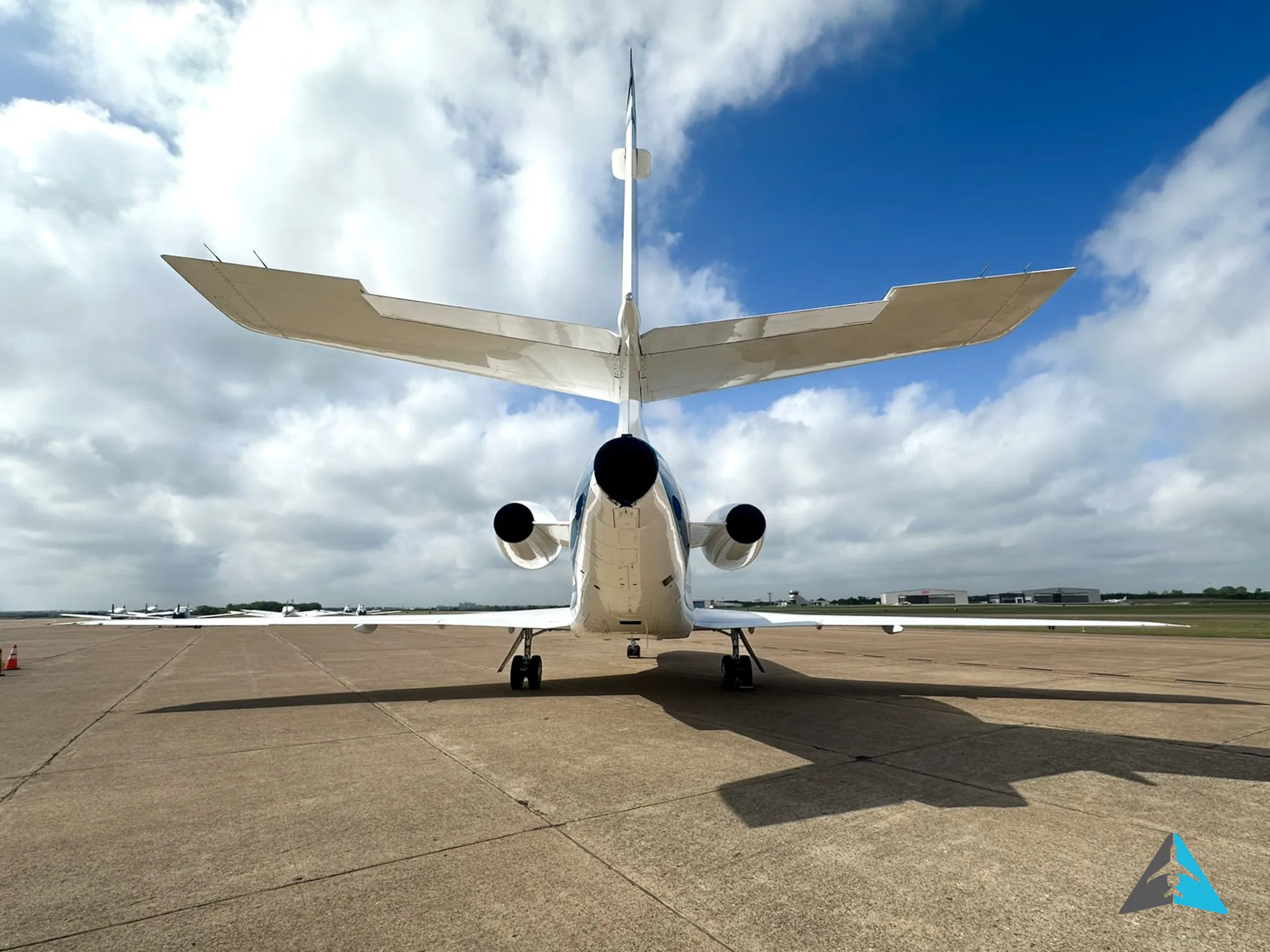 A rear view of a white Dassault Falcon 900EX business jet parked on an airfield under a cloudy sky.