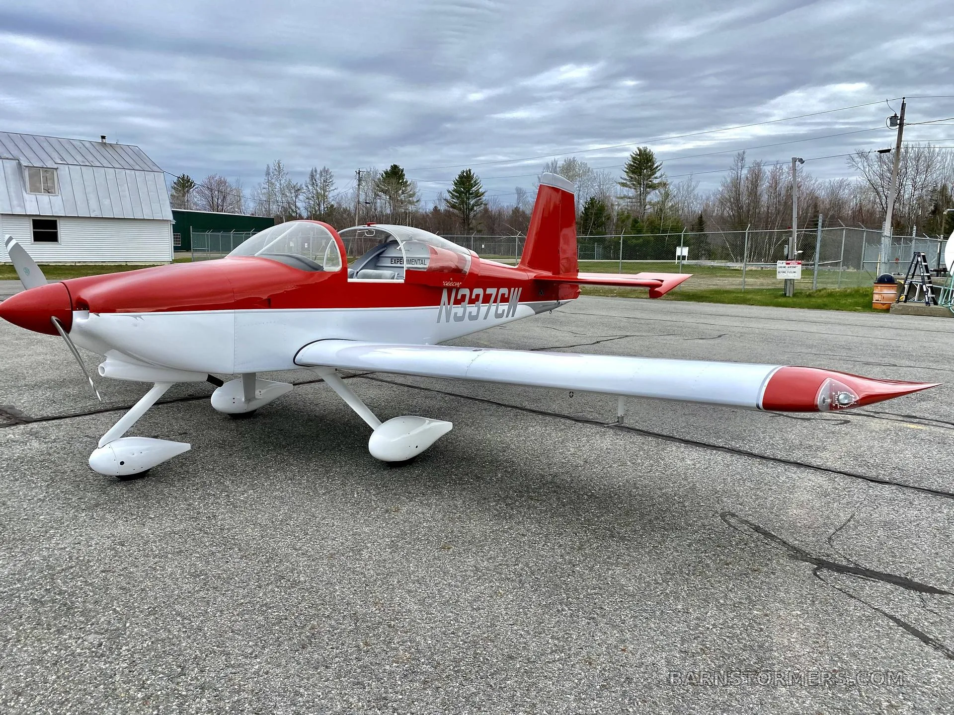 A red and white experimental aircraft with registration N337CW is parked on an airfield under a cloudy sky.