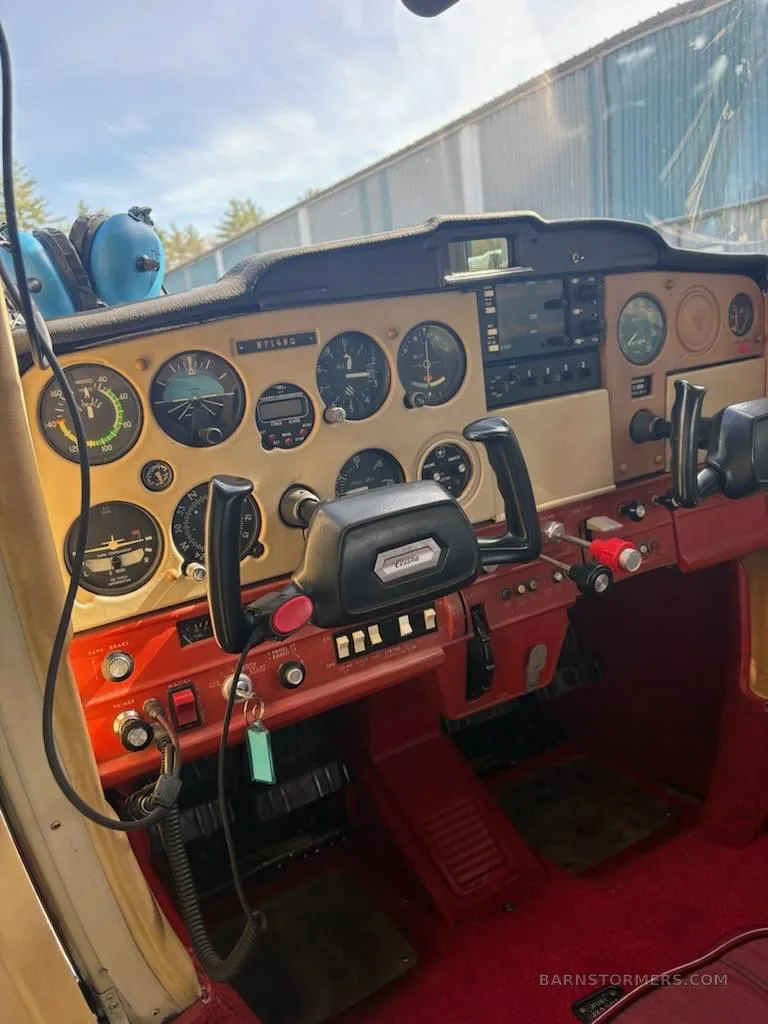 The cockpit instrument panel of a small aircraft, featuring analog gauges and a red carpeted floor.