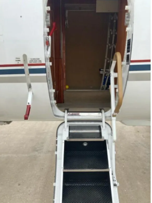 The open entry door and integrated airstairs of a white aircraft with a blue and red stripe.