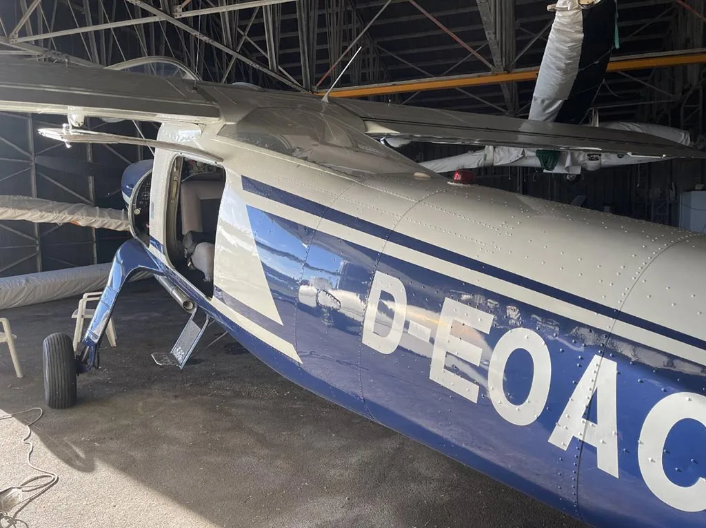 The right side of a blue and white aircraft, D-EOAC, with its door open, parked inside a hangar.