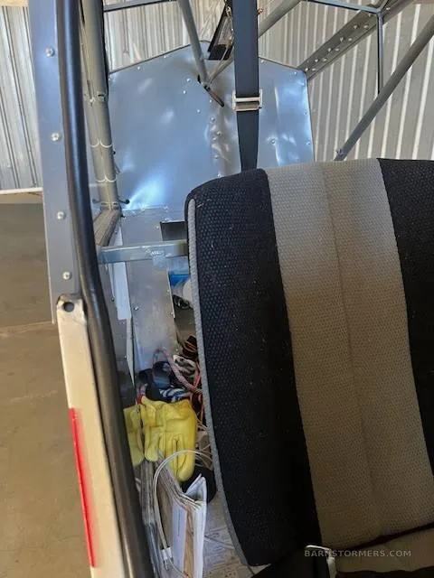 The rear interior of a small aircraft cabin, showing a black and gray seat and some items stored behind it.