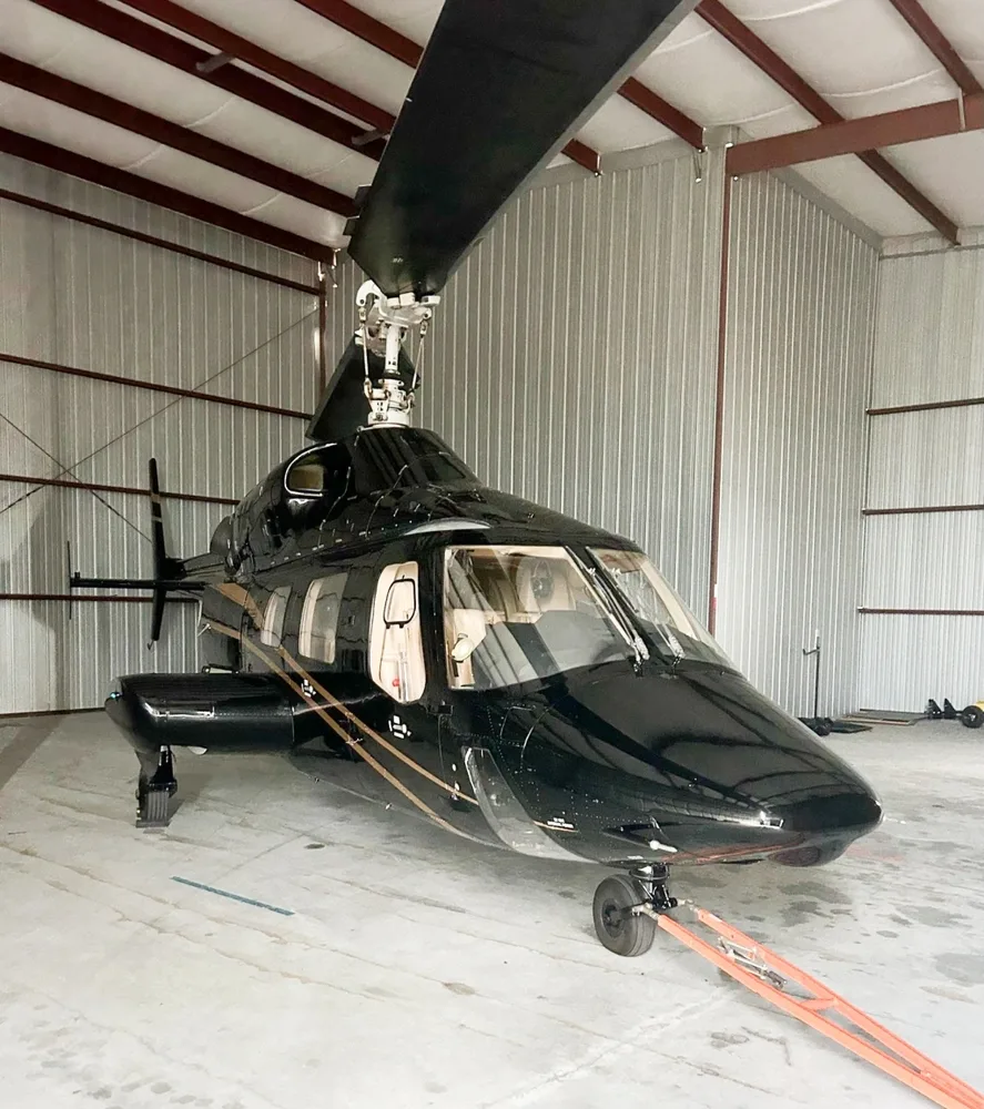 A black Bell 430 helicopter with gold stripes parked inside a hangar.
