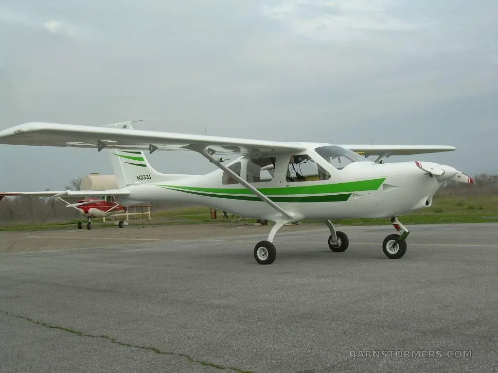A white and green light aircraft (N333J) is parked on an asphalt tarmac under an overcast sky.