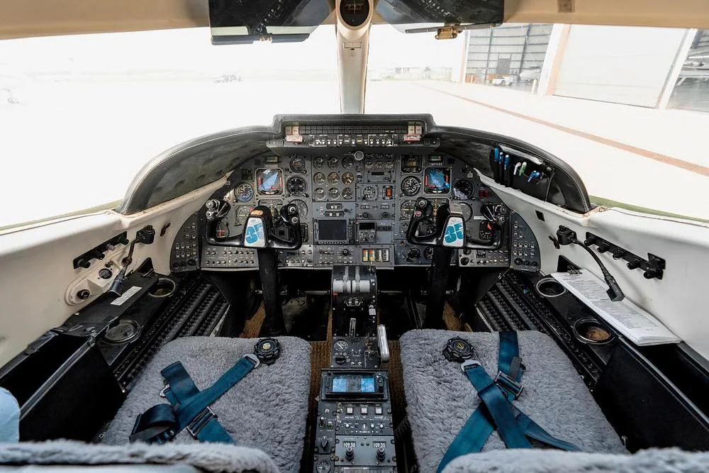 The cockpit of a private jet, featuring a complex instrument panel, dual yokes, and a central console.