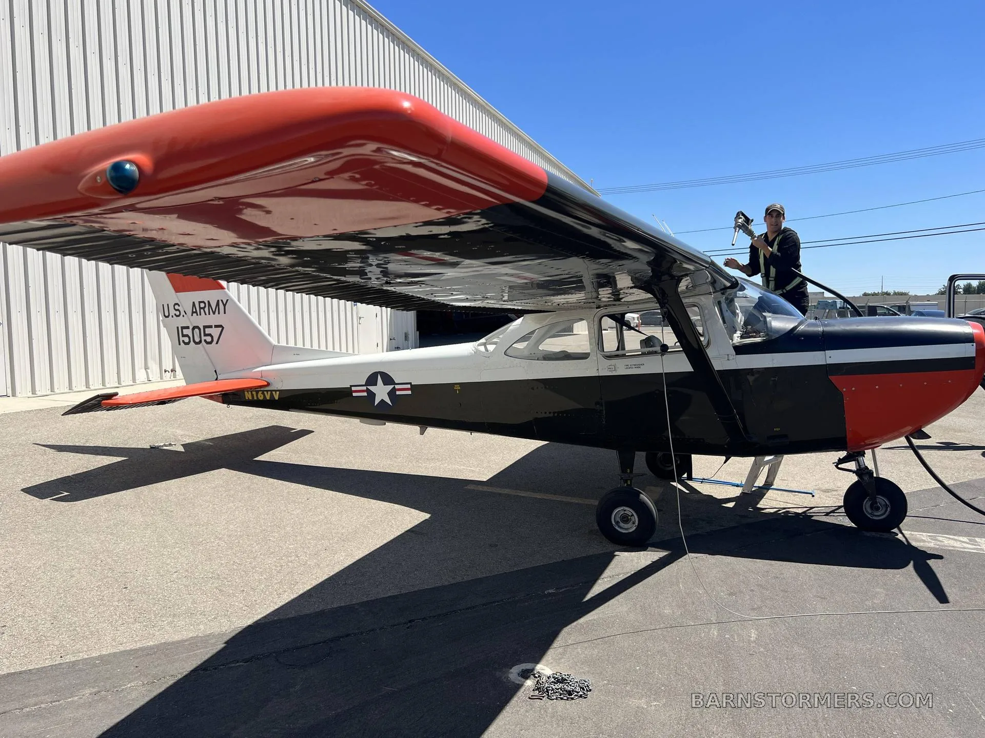 A black, white, and red U.S. Army T-41B aircraft is being refueled on an airfield next to a hangar.