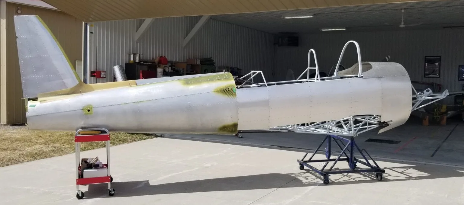 A partially assembled aircraft fuselage, with the tail section attached, sitting on stands outside a hangar.