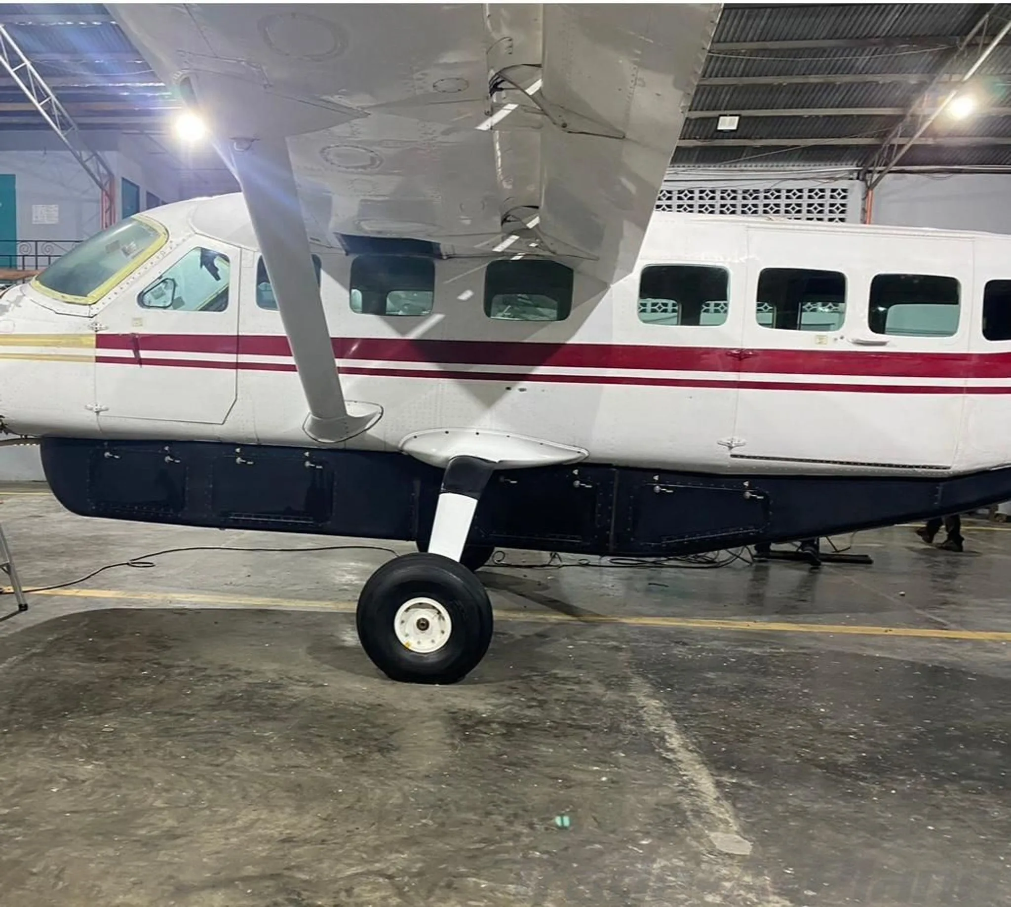 A white turboprop aircraft with red and gold stripes and a dark lower fuselage is parked inside a hangar.