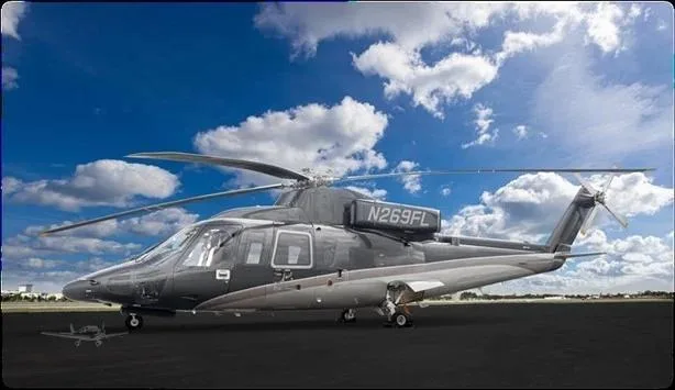 A dark grey and silver helicopter, N269FL, is parked on an tarmac under a blue sky with white clouds.