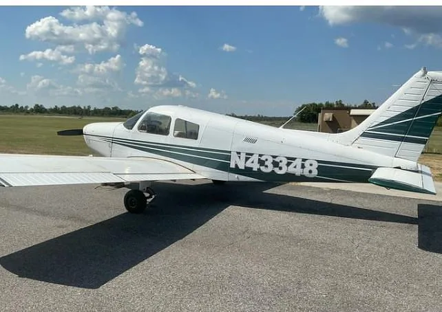 A side view of a white Piper Cherokee with green stripes, registration N43348, parked on an asphalt ramp.