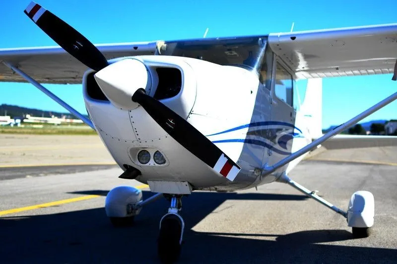 A front view of a white single-engine propeller aircraft with blue stripes on an airfield.