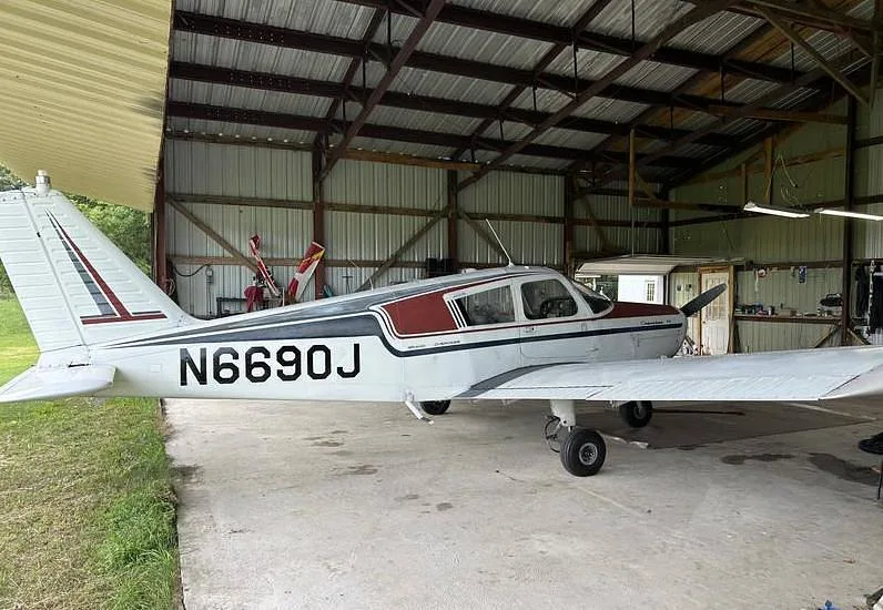 A side view of the white and maroon Piper Cherokee 140 aircraft, N6690J, parked in a hangar.