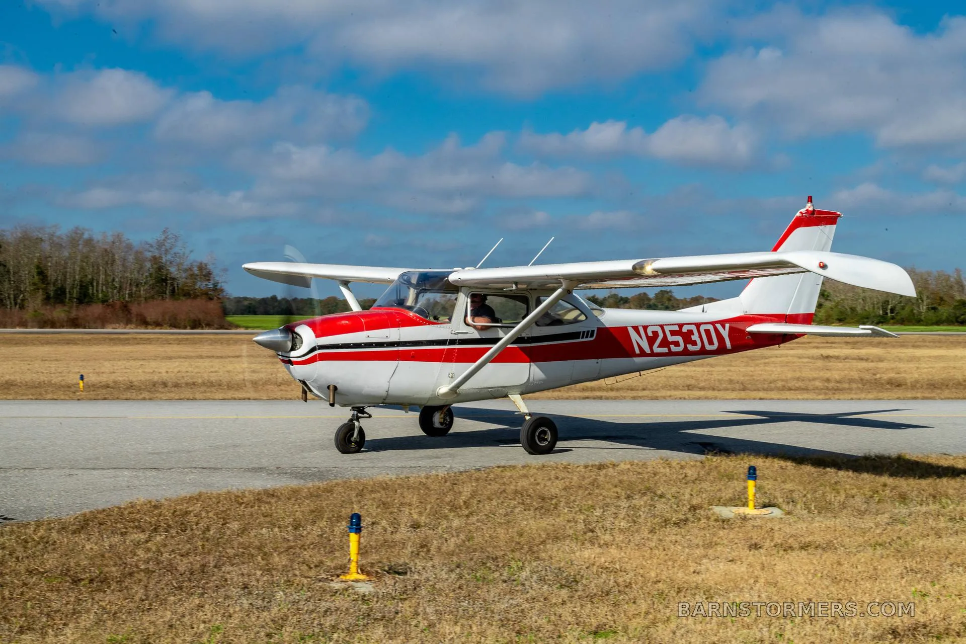 A white and red single-engine propeller aircraft, N2530Y, is taxiing on a paved surface under a blue sky.