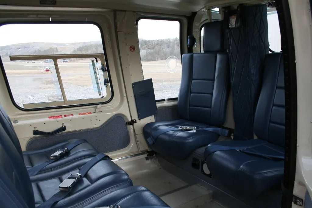 View of the blue leather passenger seats in the helicopter cabin, looking towards the front with an airfield visible outside.