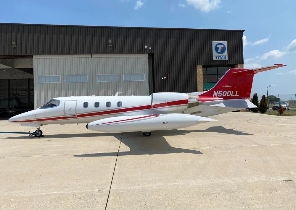 A white Learjet with red and grey stripes, registration N500LL, parked on an airfield in front of a hangar.