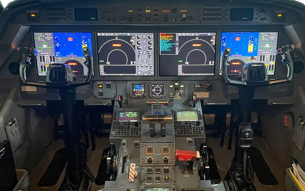A detailed view of the Gulfstream G550 cockpit instrument panel, featuring large digital displays, control yokes, and the central control pedestal.