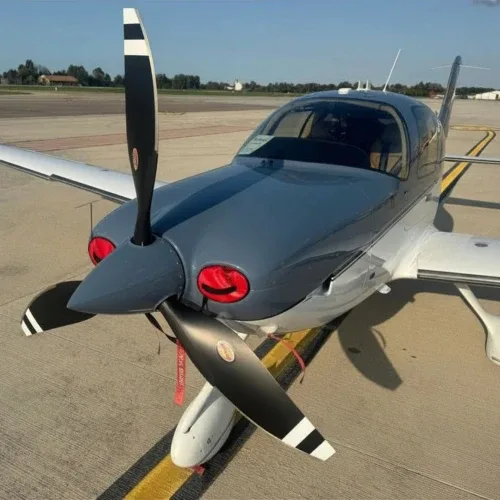 A grey and white single-engine propeller aircraft, likely a Cirrus SR22, seen from a high angle on an asphalt tarmac.