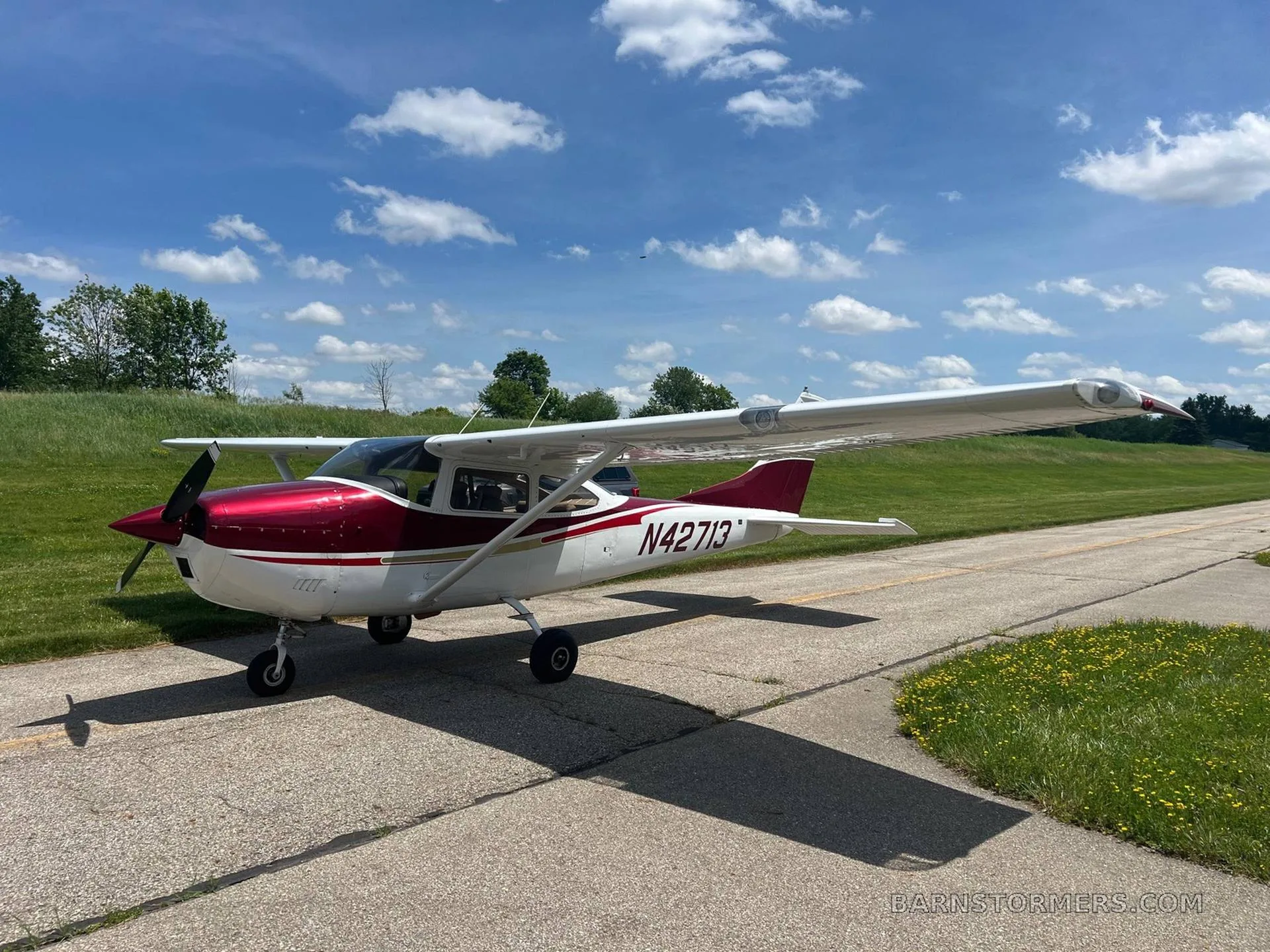 A front-quarter view of the red and white Cessna N42713 parked on an airfield with green grass and a blue sky.