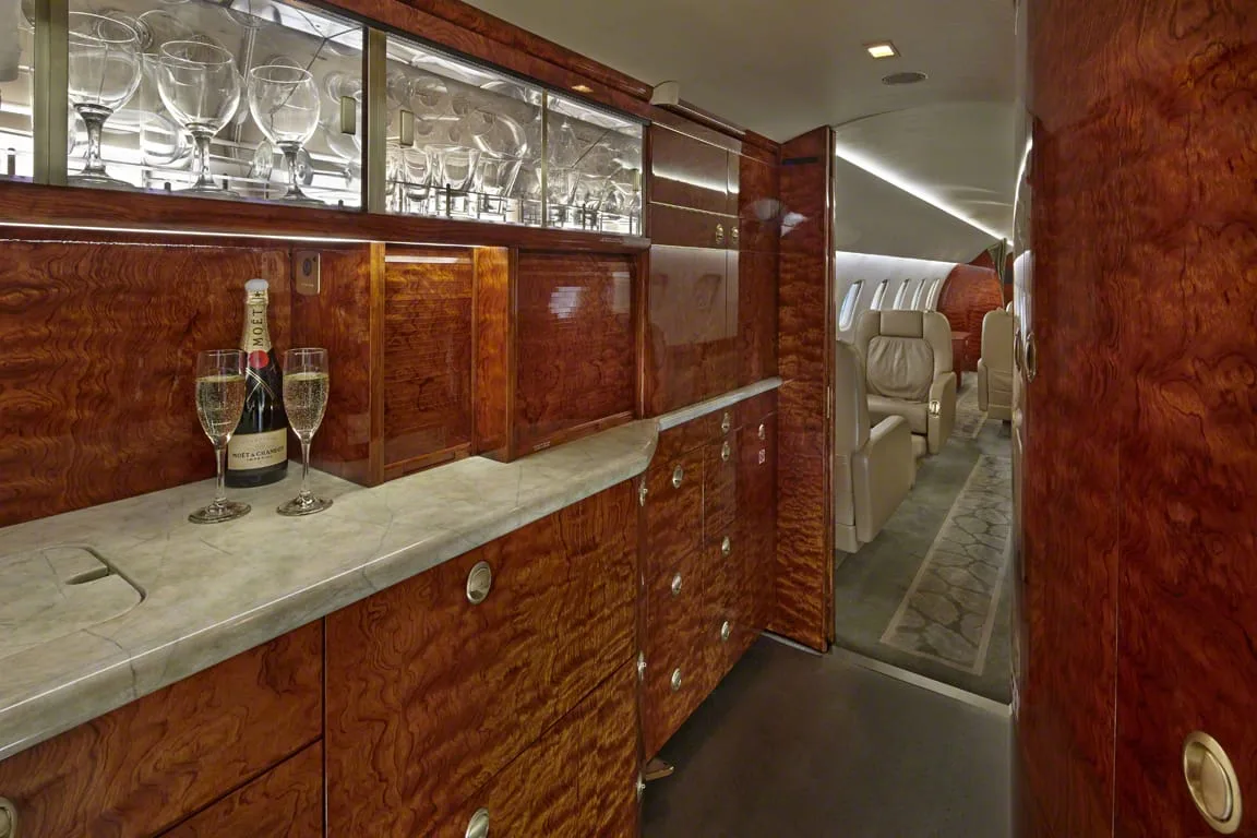 An aircraft galley area with a marble counter, wood cabinetry, glassware, and champagne bottles.