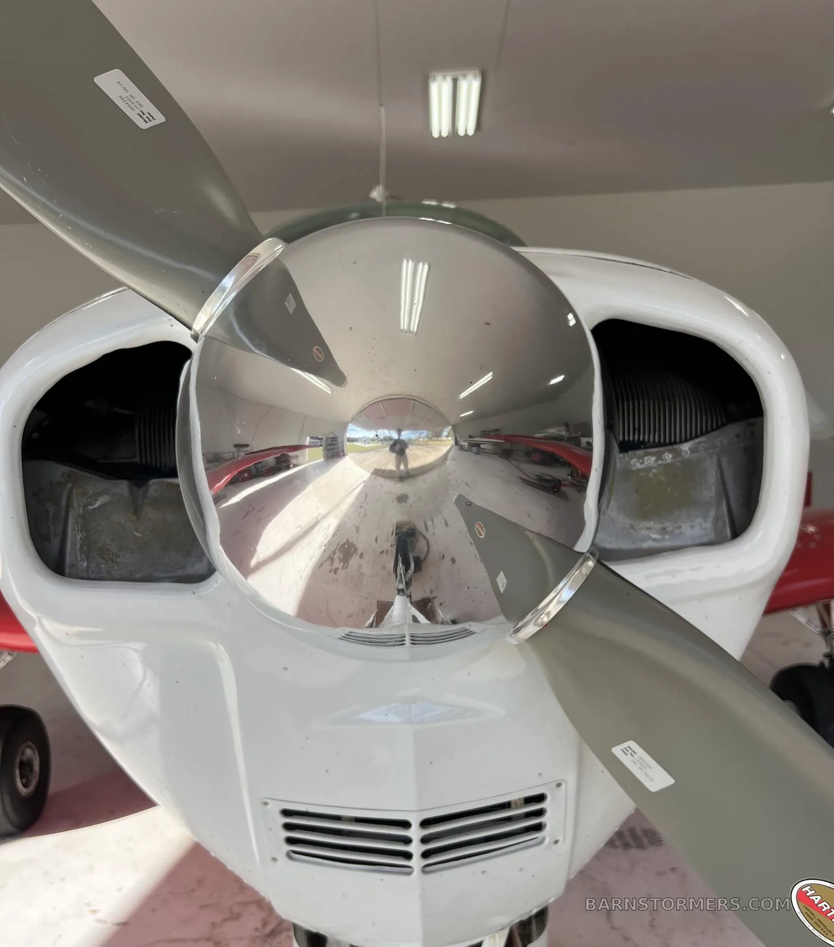 A close-up view of the polished propeller spinner and engine cowling of a red and white Beechcraft Bonanza.