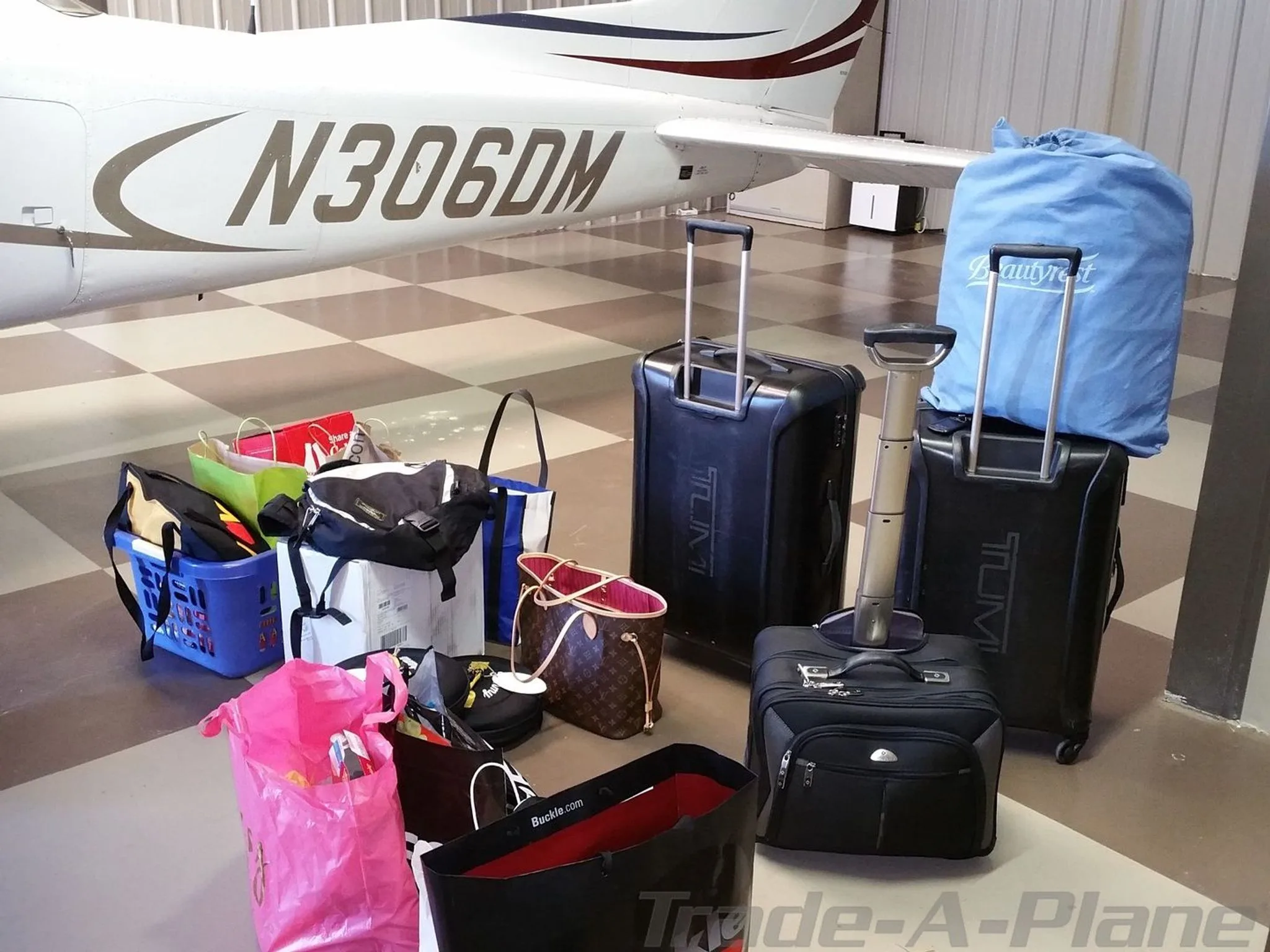 The tail section of the N306DM aircraft with various bags and luggage placed on the hangar floor nearby.