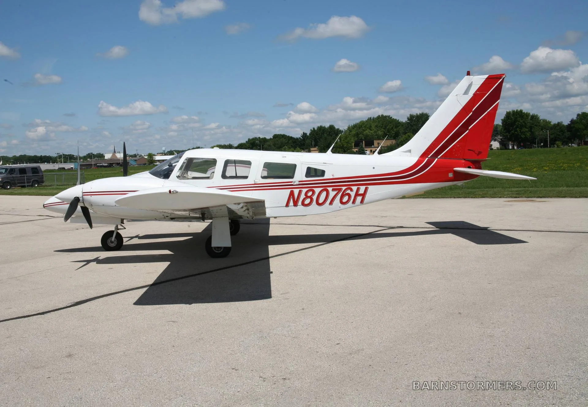 A white and red single-engine propeller aircraft with registration N8076H parked on an asphalt ramp under a blue sky.