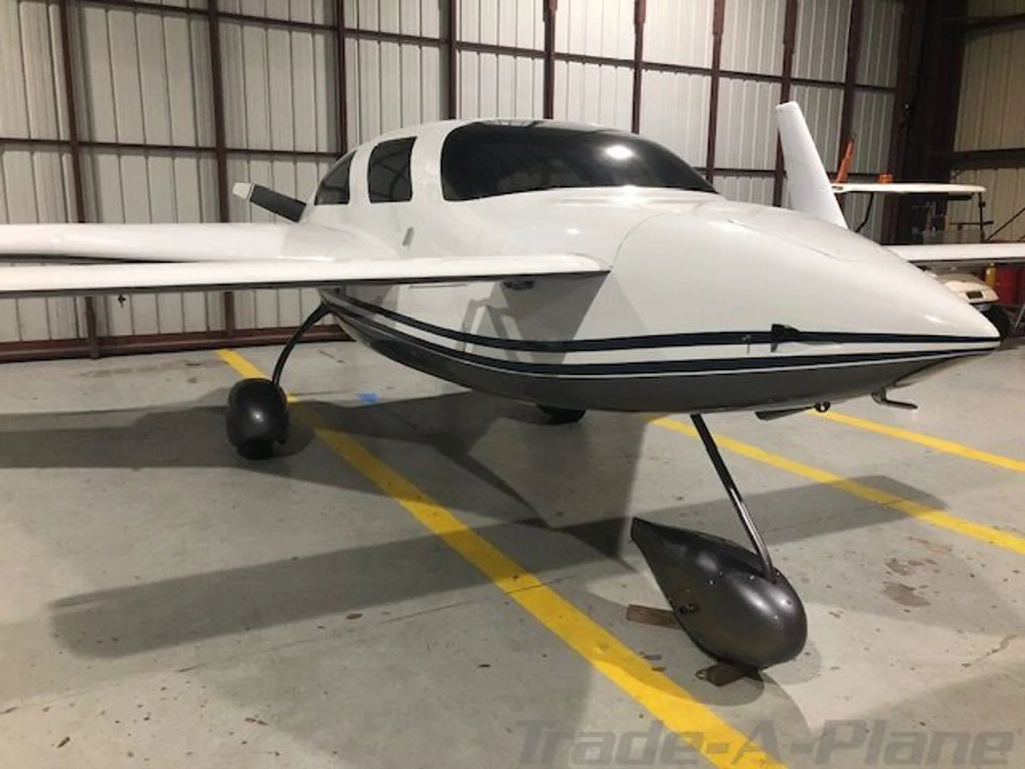 Front view of a white and dark grey Velocity aircraft with a sleek design, parked in a hangar.