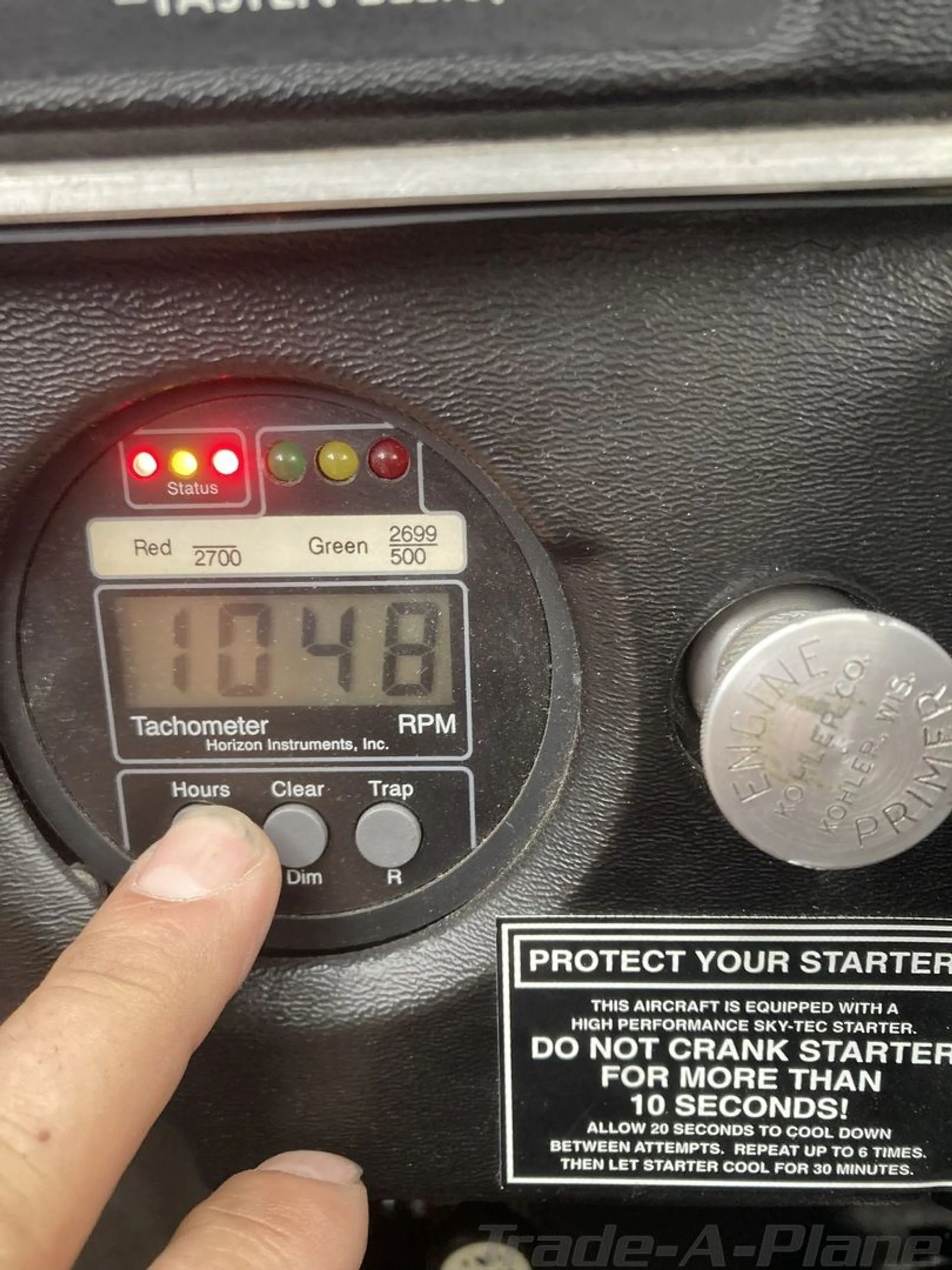 A close-up of the aircraft's tachometer showing 1048 hours and an engine primer knob.