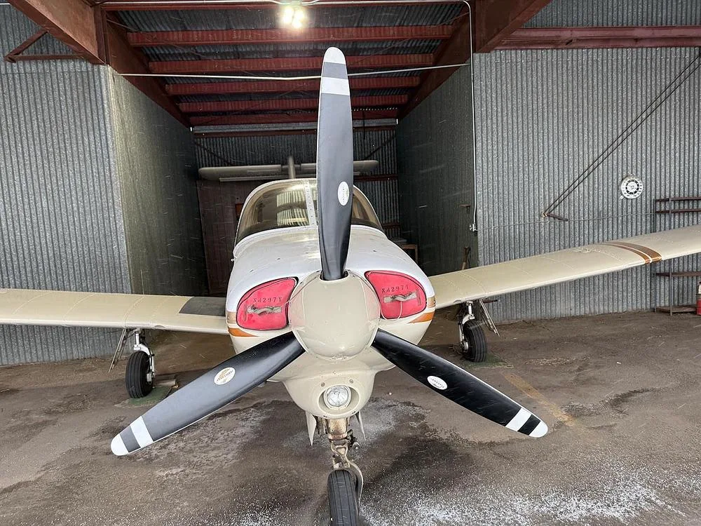 A head-on view of the Piper Arrow IV aircraft, N4297Y, showing its propeller and nose in a hangar.