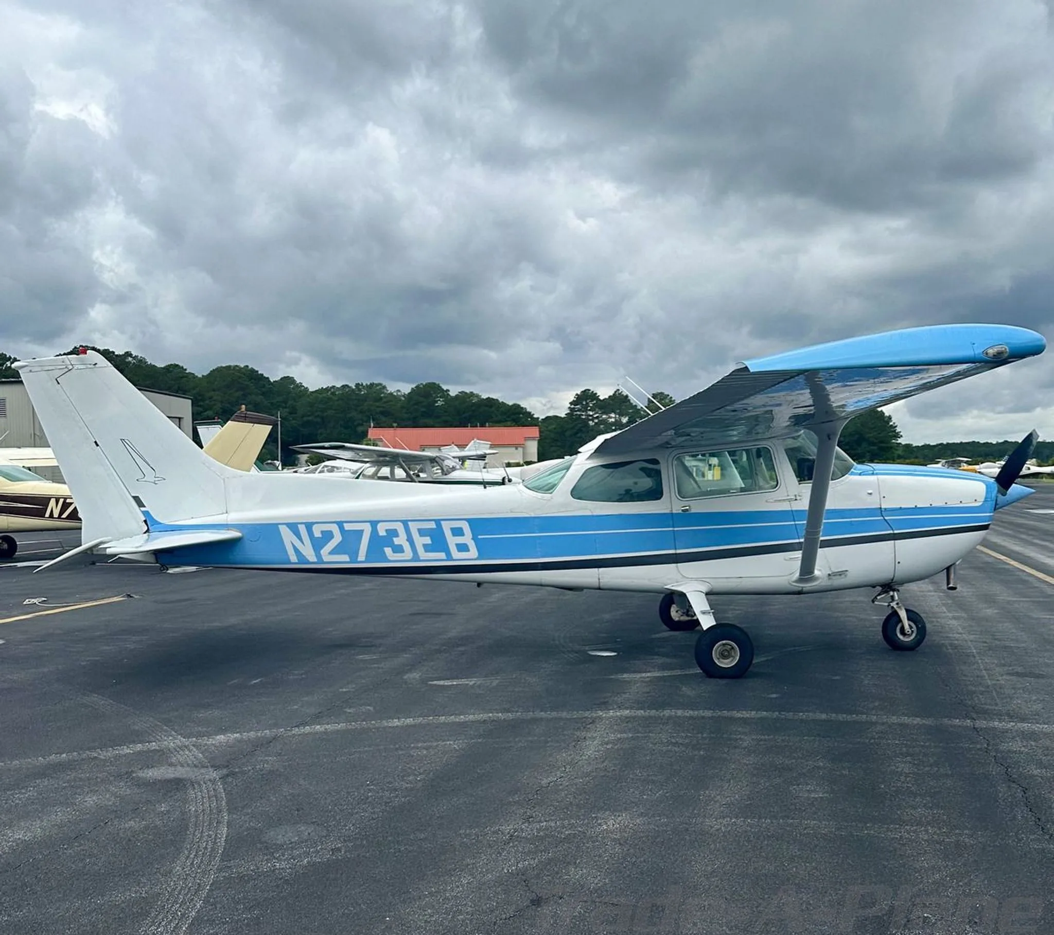 A full side view of the white and blue Cessna 172, registration N273EB, on an airport ramp.