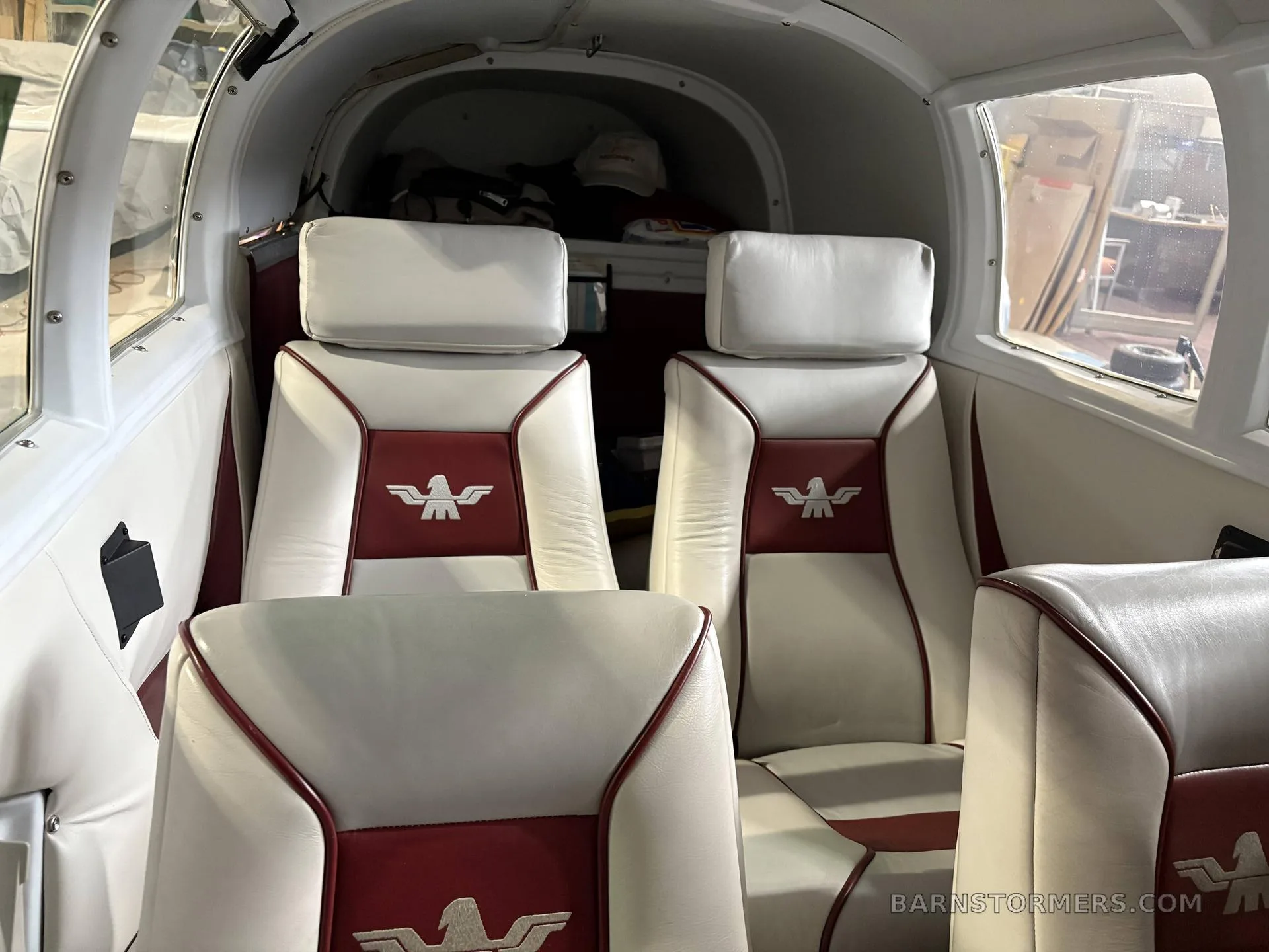 The interior cabin of a small aircraft, featuring white and red leather seats with an aircraft logo.