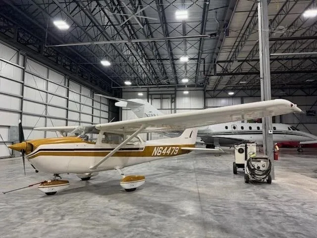 A white and gold Cessna aircraft, tail number N64479, is parked in a hangar next to a business jet.