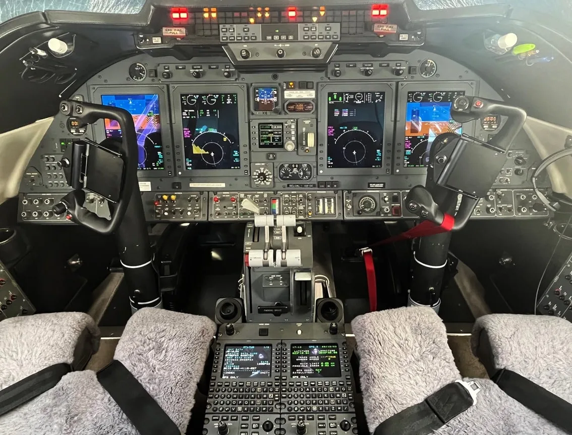 The cockpit of a business jet features multiple digital displays, control yokes, and a central throttle quadrant.