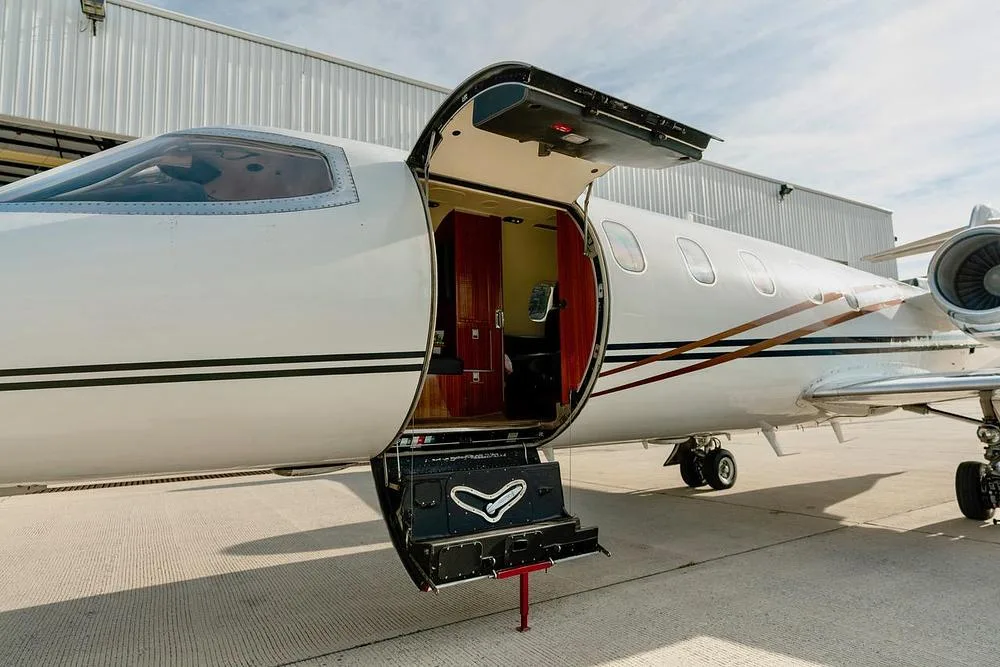 The open main entry door and integrated airstairs of a white private jet, revealing a glimpse of the cabin interior.