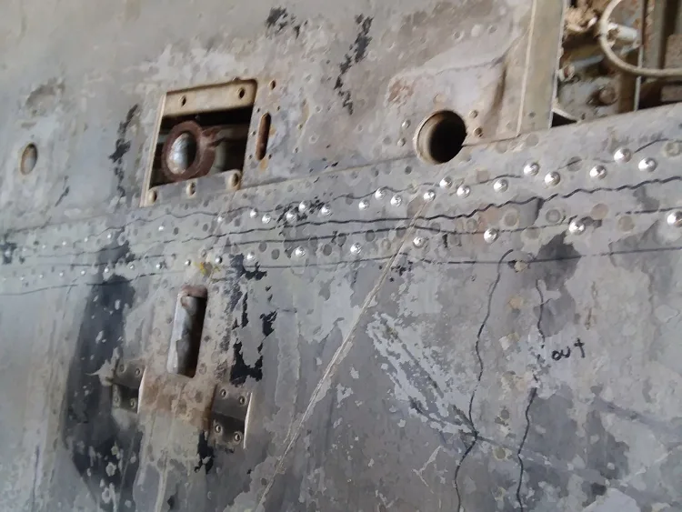 Close-up view of worn, riveted metal aircraft skin with paint remnants and markings.