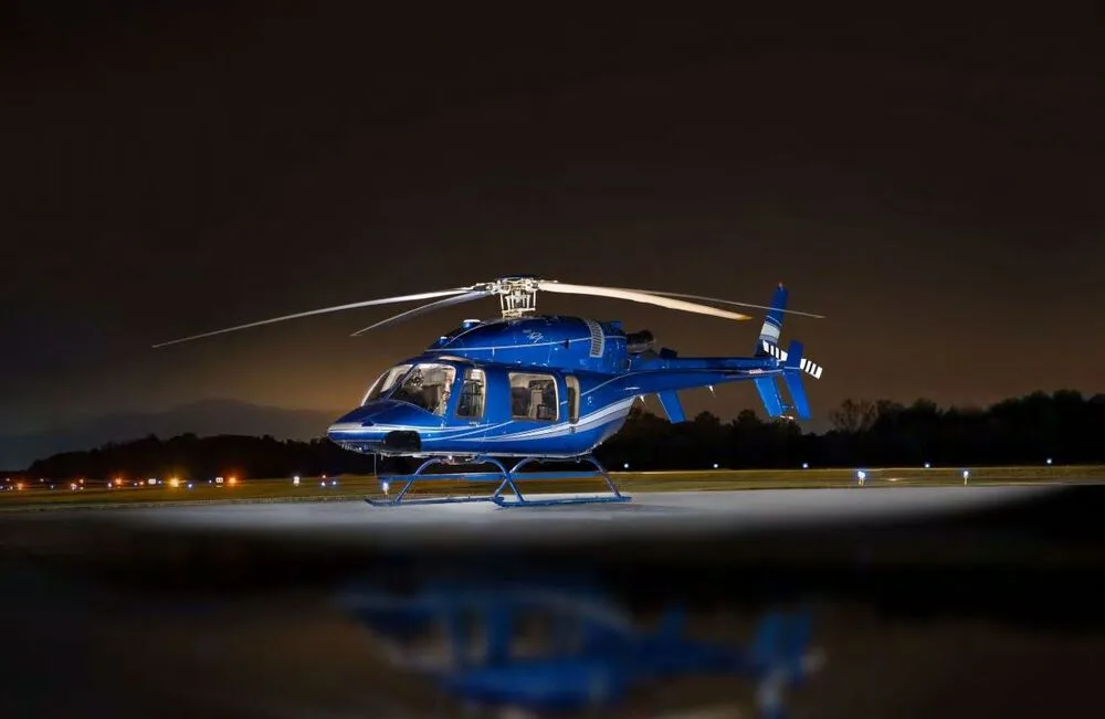 A blue Bell 427 helicopter with white and silver stripes is parked on an illuminated runway at night.