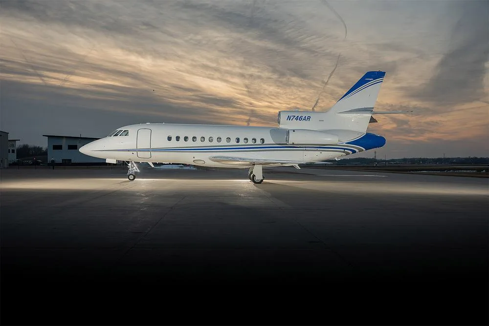 A Dassault Falcon 900EX business jet with registration N746AR sits on an airport tarmac at sunset.