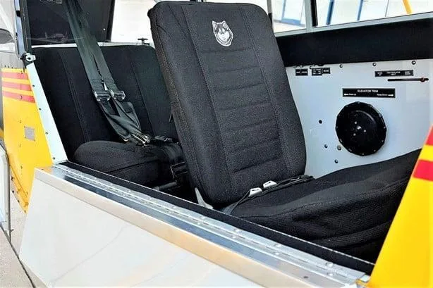 The black fabric seats of an Aviat Husky A-1C aircraft cabin are visible, with a Husky logo on the seatback.