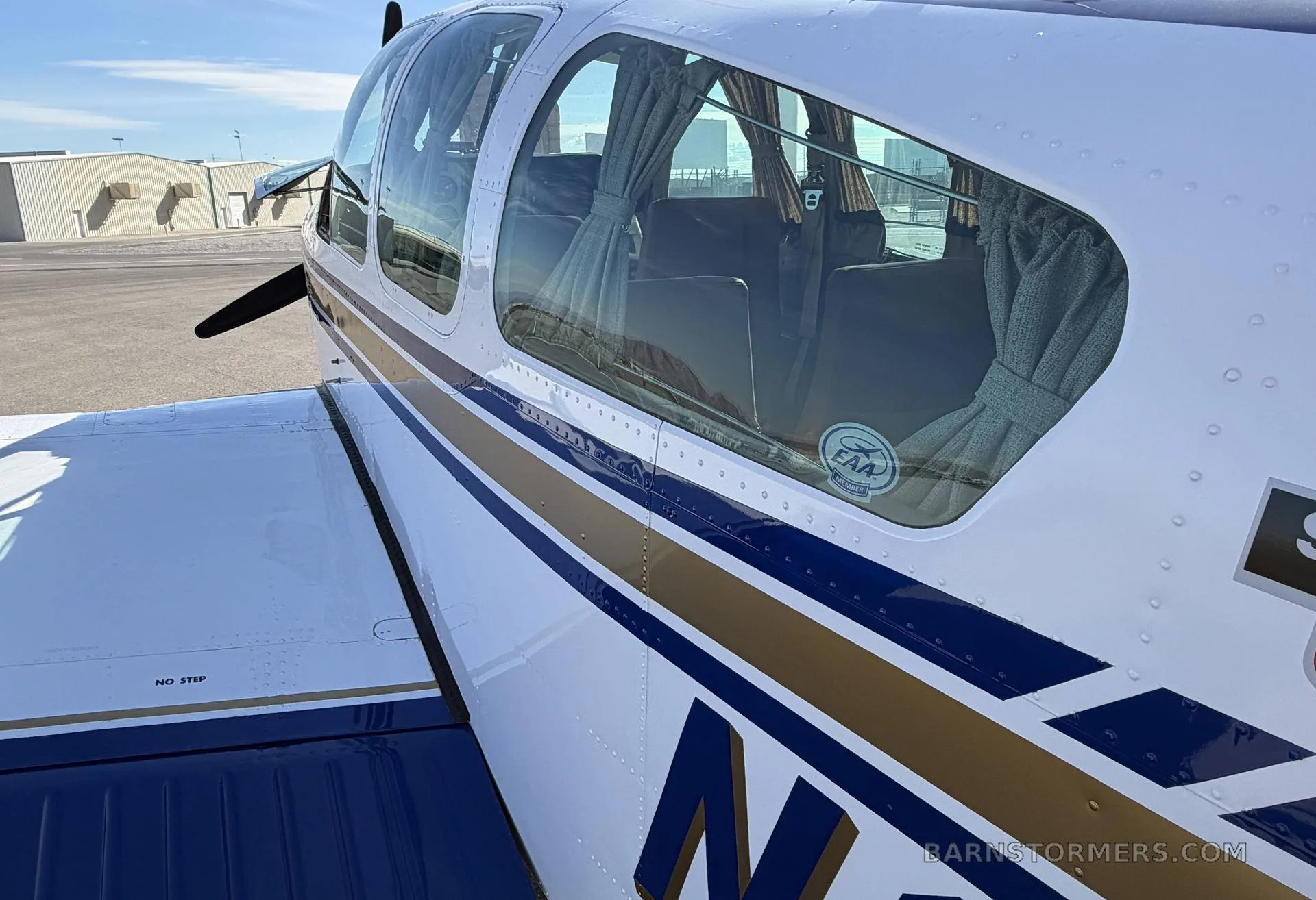 A close-up of the fuselage of the white, blue, and gold Beechcraft Bonanza N68550, showing the cabin through the window.